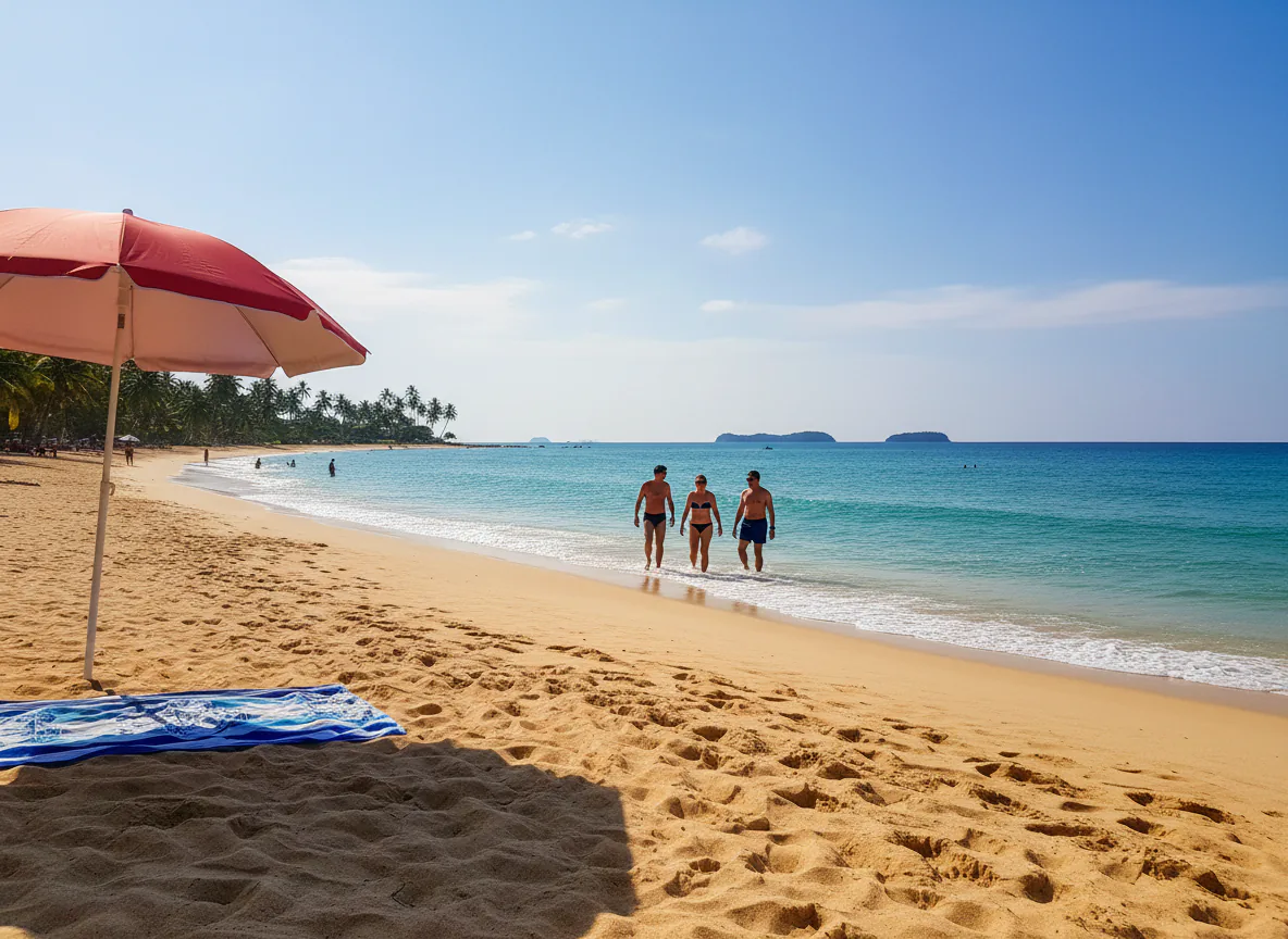 Sunny beach with a red umbrella and a towel in front and a group of people walking along the water in the background
